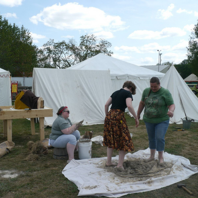 several modernly-dressed people squish mud with their feet to make the material to build an oven.